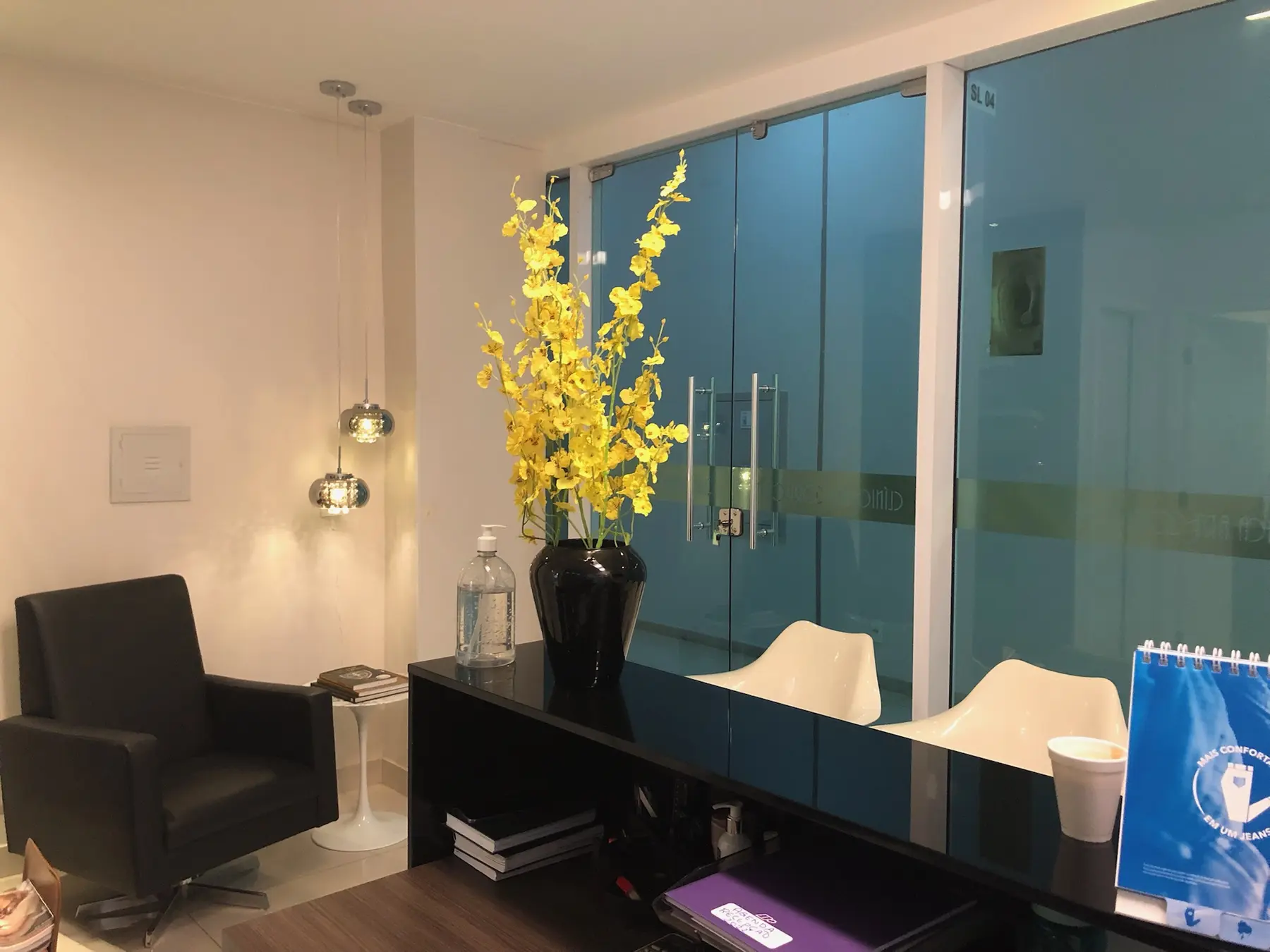 Recepção da Clínica Art Corporis, com arranjo de flores amarelas e divisórias de vidro.