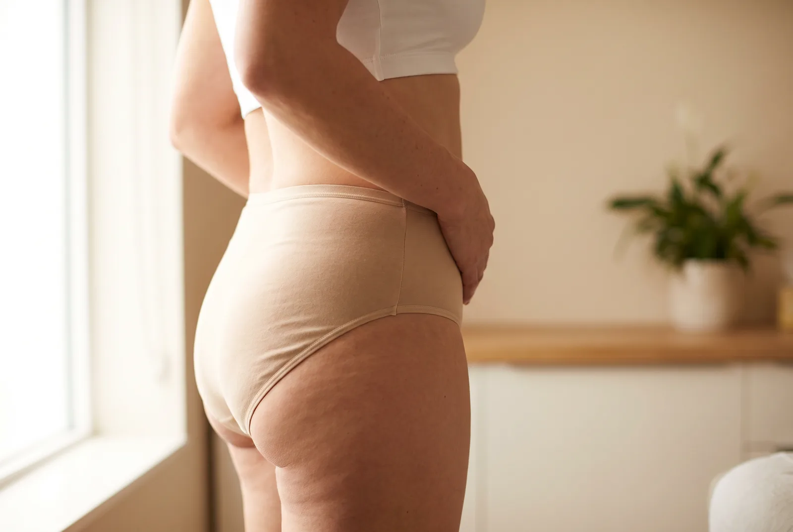 Mulher de lado com a mão apoiada no baixo ventre, região da cicatriz de abdominoplastia.